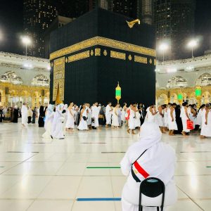 Muslim pilgrims perform Tawaf around the Kaaba in Mecca under bright lights at night.